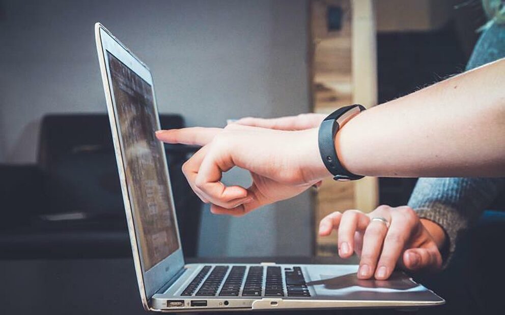 Two people pointing at a laptop screen.